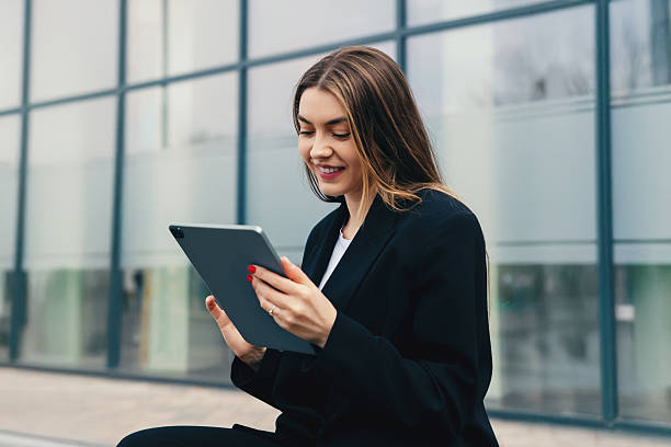 istock Professional Woman Smiles While Using Tablet Outside Modern Building During Daytime 2242068322