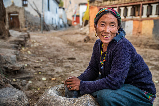 Tibetan woman using a stone mortar to make flour, small village in Upper Mustang. Mustang region is the former Kingdom of Lo and now part of Nepal,  in the north-central part of that country, bordering the People's Republic of China on the Tibetan plateau between the Nepalese provinces of Dolpo and Manang.