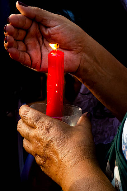 istock A human hand holds and protects a lit red candle, its flame glowing against the dark background. 2242074739