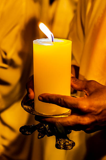 A human hand holding a lit candle in a soft golden light, suggesting a ritualistic or contemplative moment.