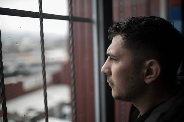 istock Portrait of Young Middle Eastern Man Looking Out Rainy Window with Emotional Expression – Stock Photo 2242076872