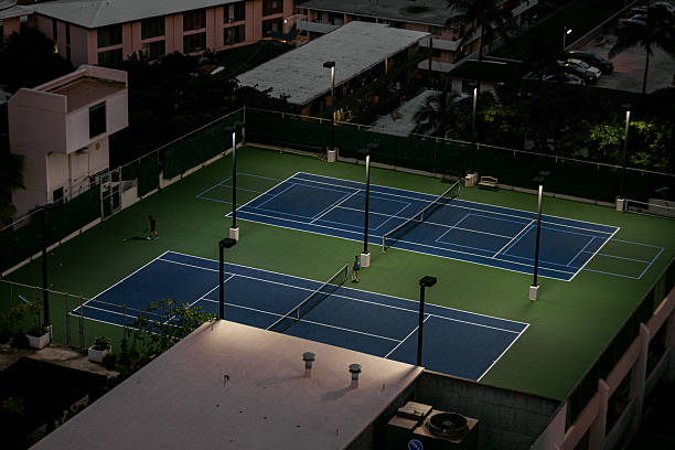 Evening tennis game on illuminated rooftop courts, top view, atmospheric urban scene with soft lamp light and players against residential buildings
