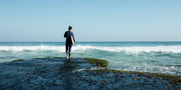 Woman surfer with surfboard going to surf at seaside
