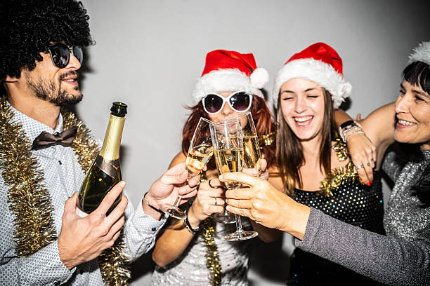 A cheerful group of friends wearing festive hats and accessories, toasting with champagne glasses, capturing the joy and camaraderie of a holiday celebration.