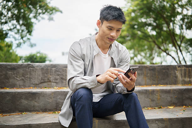 istock Adult asian man checking messages on mobile device during a break outside. 2242091501