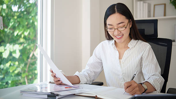 istock Asian businesswoman reviewing documents and taking notes at a bright office desk. 2242091823