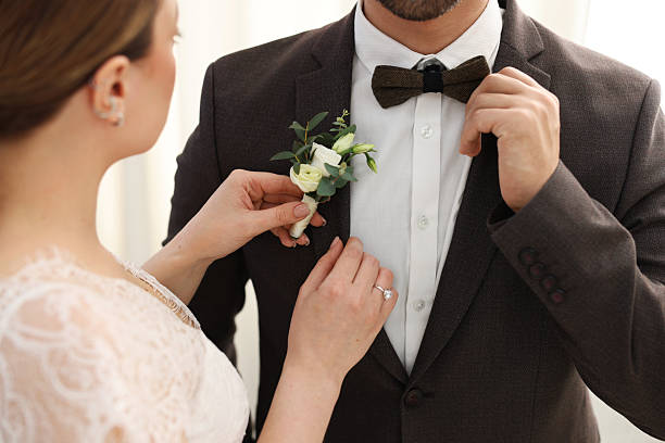 istock Bride putting boutonniere on her groom's jacket against light background, closeup. Wedding accessory 2242096010