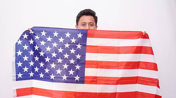 Asian Fat Man wearing yellow t-shirt holding USA flag at studio against white background.
