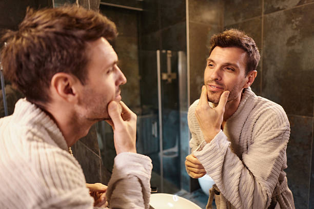 istock Smiling man looking his complexion in a mirror at bathroom. 2242118777