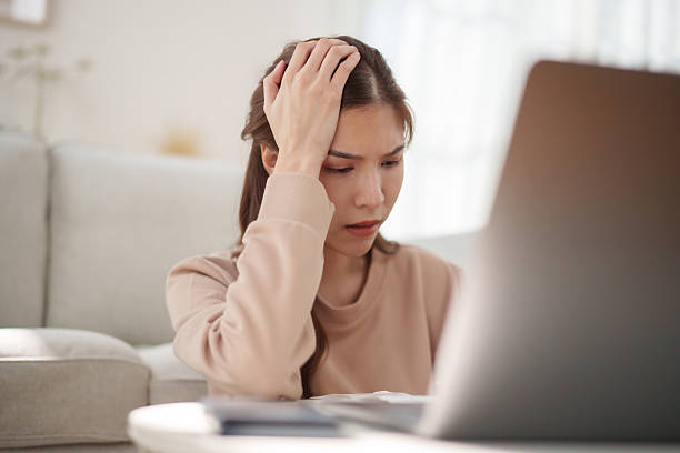 istock Upset Asian woman with hand on her head, feeling stressed and frustrated while checking bills and financial issues at home. 2242118926