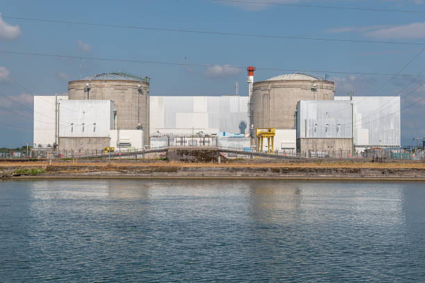 istock Industrial nuclear facility by waterfront under clear sky with distant clouds and power lines 2242123027