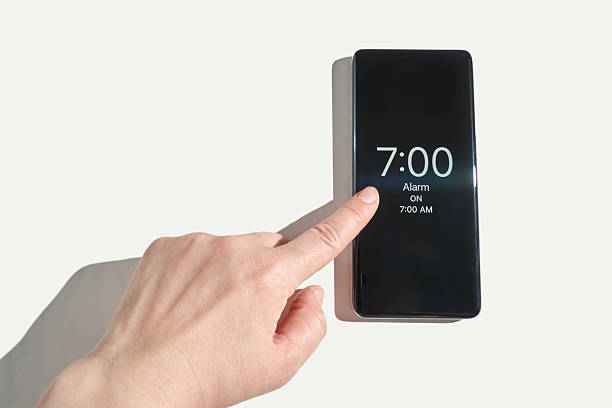 istock Adult caucasian hand setting alarm clock on smartphone device against white 2242124036