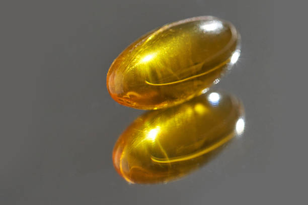 Close-up of single soft gel capsule with reflection on shiny surface.
