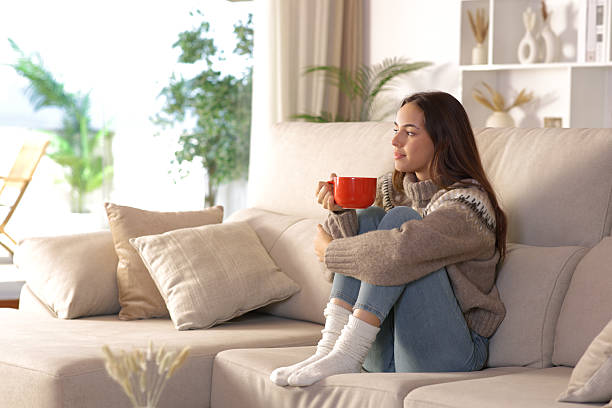 istock Woman in winter drinking coffee looking through a window 2242125443