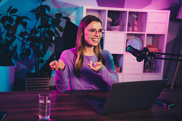 istock Young female blogger creating content in neon-lit home office studio with laptop and microphone, showcasing creativity 2242127074