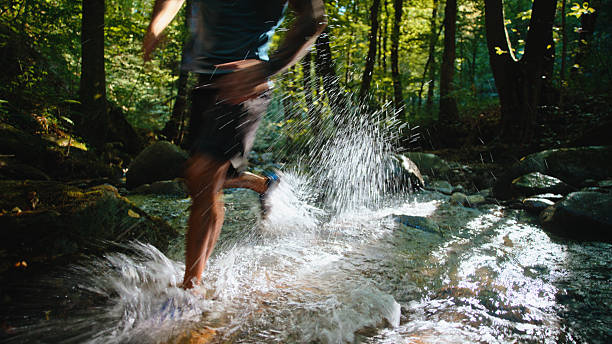 Male Runner Maintaining an Active Lifestyle,Exercising Outdoors by Traversing a Rocky Forest Creek,Creating Dynamic Water Splashes in a Natural Environment