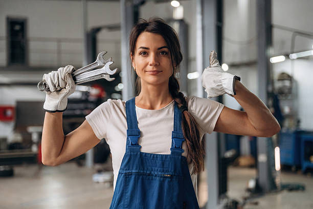 Cute girl with funny pigtails dressed in overalls sitting in the trunk of a pickup truck in a car repair shop. A boy is repairing the pickup behind her