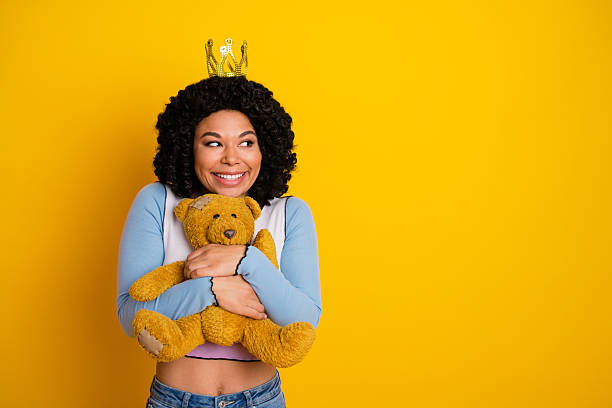 istock Young woman with thoughtful expression hugging a teddy bear against a vibrant yellow background 2242128720