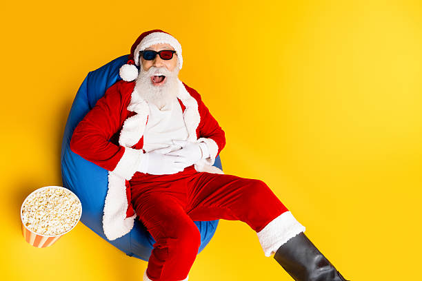 istock Santa Claus Relaxing on a Beanbag Holding Popcorn on Bright Yellow Background 2242129936