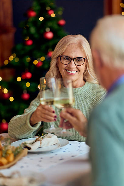 istock Smiling Senior Couple Toasting With Wine Glasses During Christmas Dinner By Tree 2242130332