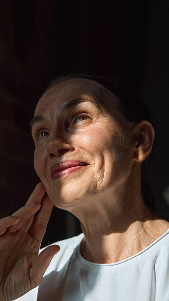 Elderly woman touching face with gentle smile under sunlight