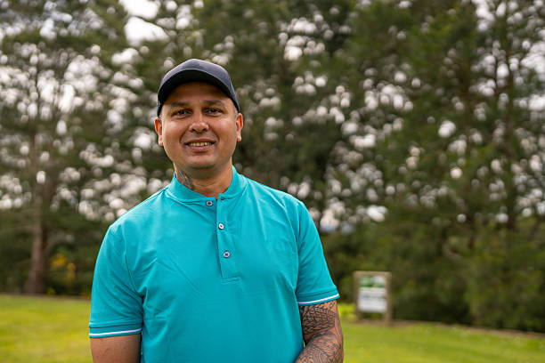 A South Asian male golfer smiles while standing on a golf course