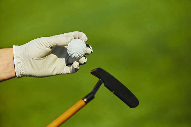 Golfer hand in a glove puts a golf ball on the tee in the field
