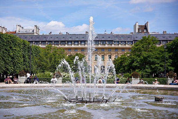 Water fountain in Paris garden on sunny day with classic building