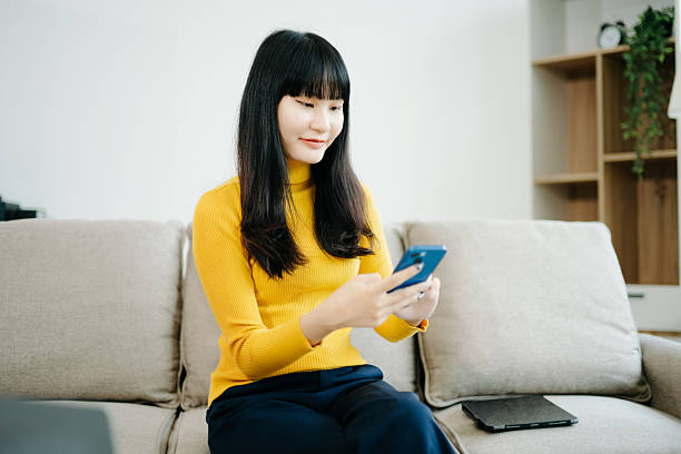 istock Young asian woman relax on comfortable couch at home texting messaging on smartphone and tablet 2242144241