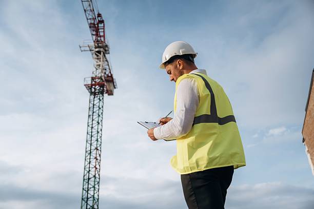 istock According to a plan. Construction site worker is against building crane and sky background 2242147475