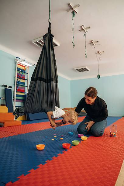 istock Control of the balance. Doing exercises. Preschool child with teacher during developmental activities in a playroom 2242149681