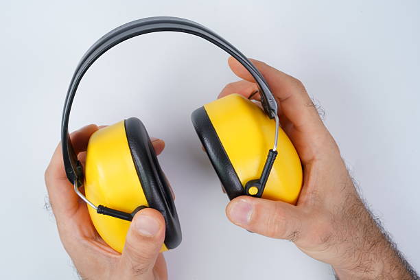 A person holds yellow ear protection gear with a black band, commonly used to reduce noise in construction sites or loud events, standing against a plain white background.