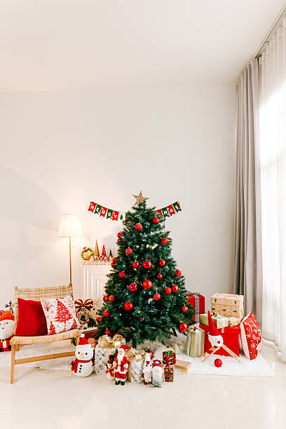 Bright living room with decorated Christmas tree, red and white ornaments, gifts, and festive decor by a window, creating a cozy holiday atmosphere.