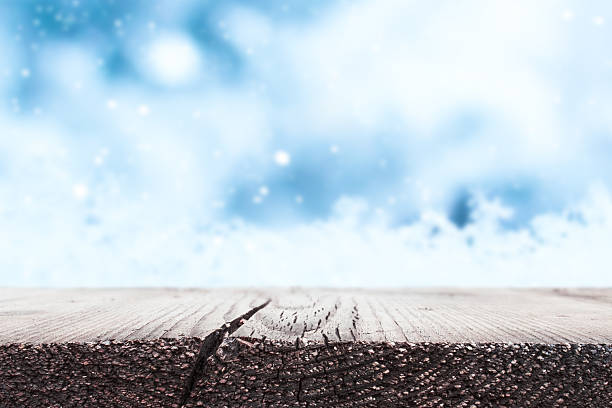 A rustic wooden table against a blurred winter sky and snowflakes. Product display surface.
