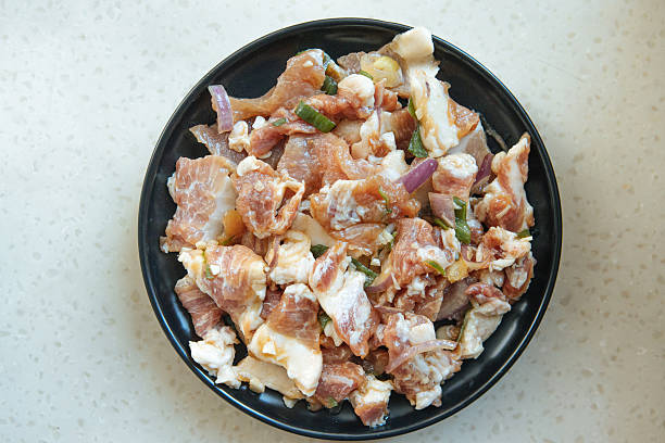 Marinated raw pork slices with seasoning and herbs on kitchen table, representing traditional food preparation, homemade cuisine, meat preservation, and authentic cooking ingredients for healthy lifestyle and culinary culture.