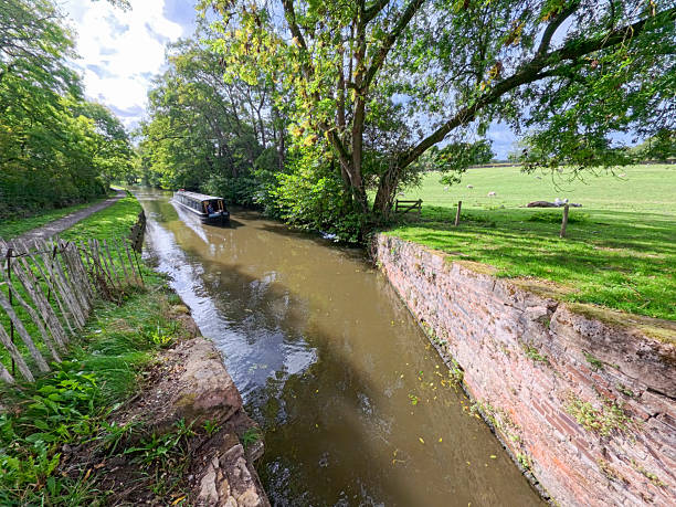 Narrowboat travelling along an English rural countryside scenery on British waterway canal with blue sky in autumn fall