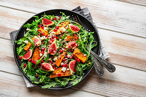 Delicious and tasty arugula and quinoa salad with figs, baked vegetables, pomegranate and greek cheese on white table. Healthy autumn vegetarian recipe. Vegan fruits and vegetable fall salad