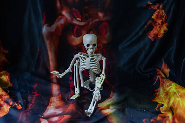 Decoration for Halloween: two skeletons hanging from a black cloth on a red background in a dark room. One skeleton in a black cape with a white bow.