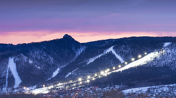 istock Evening panorama mountain ski resort. illuminated ski slope with burning lights during a beautiful lilac sunset. A serene and tranquil twilight settles over the picturesque snowy mountains, showcasing ski trails 2242166119