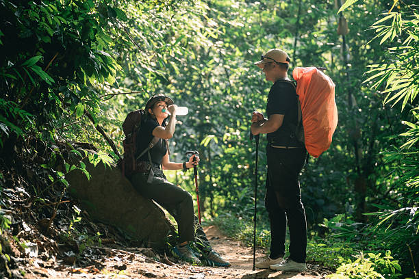 istock Adventurous hikers taking a break in lush green forest while one drinks water and other holds a walking stick surrounded by vibrant nature 2242167656