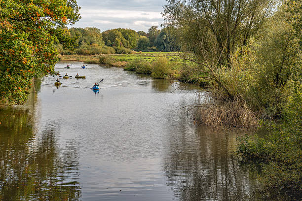 A narrow Dutch river on a cloudy autumn day. In the background, a group of people in inflatable canoes approaches.