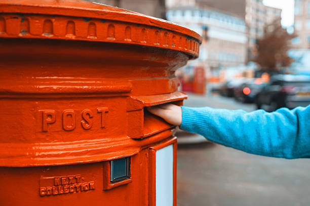 istock Hand placing letters into red post box in urban setting during daytime 2242170688