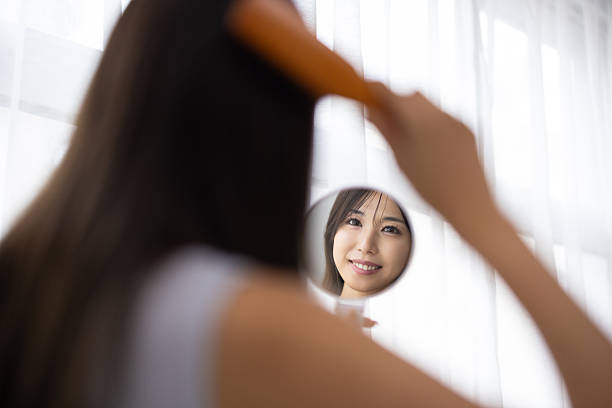 Young Woman Brushing Her Hair While Holding a Hand Mirror