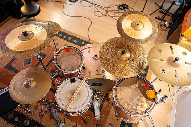 A drum kit captured from above, showing the instruments, connecting cables, and a carpeted floor beneath in a music studio setting.