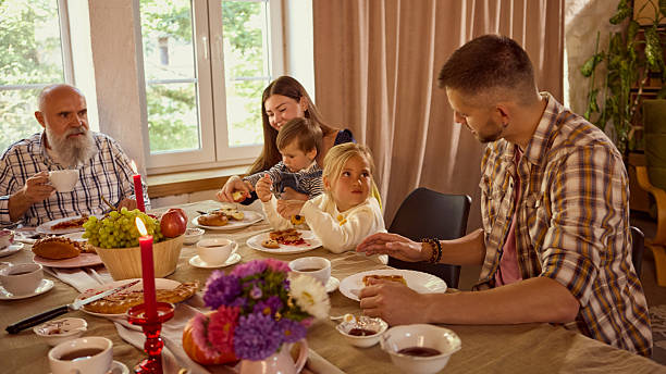 Grandfather drinking tea with grandchildren at cozy holiday family table. Concept of cultural holidays, emotional joy, wellness, and support programs reflecting love and care.