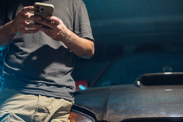 istock Man Leaning on Red Car Using Smartphone in Dimly Lit Garage for 2242178259
