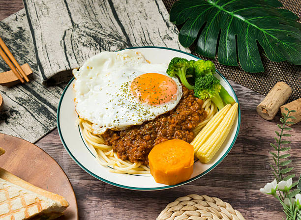 spaghetti dish, Dry Curry Beef Pasta topped with rich meat sauce and a perfectly cooked egg. The vibrant vegetables add a touch of freshness to this delightful meal.