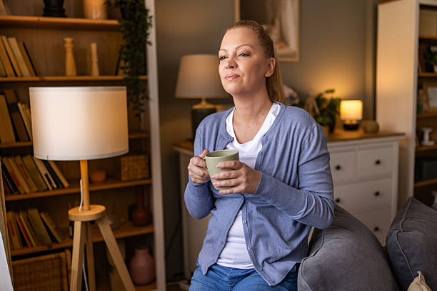 istock Beautiful woman refreshing and clearing her mind while holding mug with tea and sitting on the sofa near the window. 2242183888