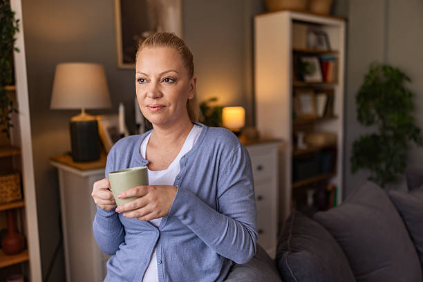 istock Beautiful woman refreshing and clearing her mind while holding mug with tea and sitting on the sofa near the window. 2242184088