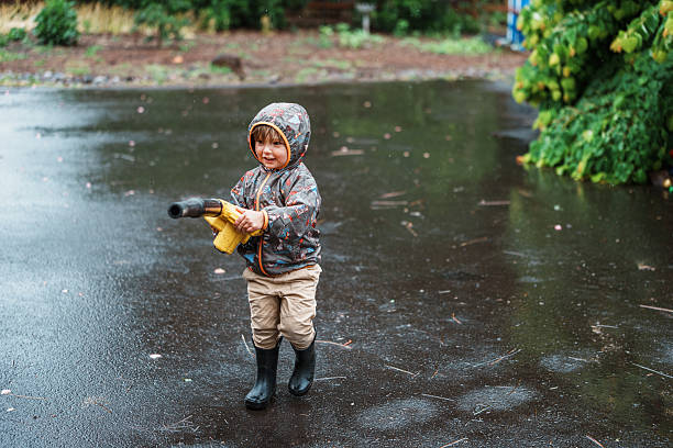 A smiling two-year-old boy has fun using a small electric leaf blower while helping is family with yard work on a rainy afternoon in rural Oregon.